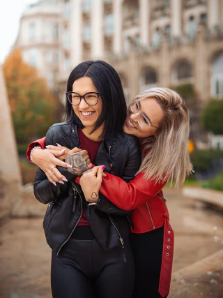 Two friends embracing and laughing, one wearing a black coat and the other a red coat