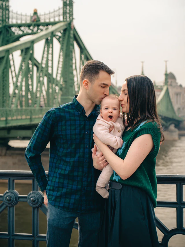 Parents holding their baby with Liberty Bridge behind them
