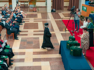 Diplomaosztó ünnepség egy tágas aulában, ahol egy végzős hallgató a színpad felé sétál.