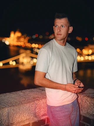 Világos pólós férfi esti portréja Budapest kivilágított látképével