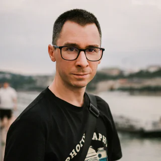 Roland Szabó wearing glasses and a baseball cap in a park at sunset.