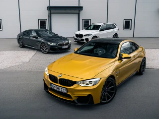 Arany, szürke és fehér BMW-k egy ipari épület előtt.