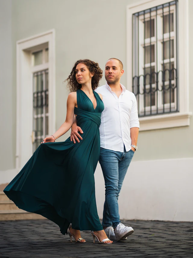 Portrait of an elegant couple walking in front of a bright building, with the woman wearing a long green dress and the man a white shirt