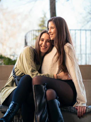 Two friends sitting outdoors with their arms around each other and smiling