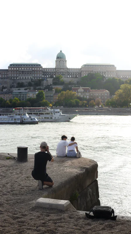 Roland Szabó photographs a couple sitting beside the Danube, with Buda Castle in the background.