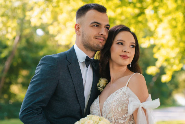 A bride and groom embracing in a sunny park.