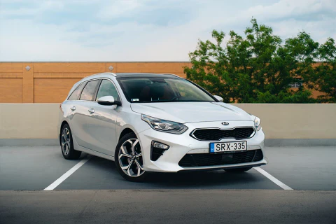Fehér Kia Ceed kombi egy szabadtéri parkolóban.