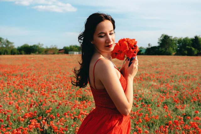 A woman in a red dress standing in a poppy field while holding poppies