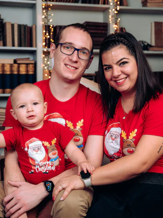 A family of three wearing red Christmas shirts while sitting on a sofa