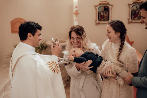Pap áldást ad egy nő karjában tartott csecsemőre egy templomi szertartáson.