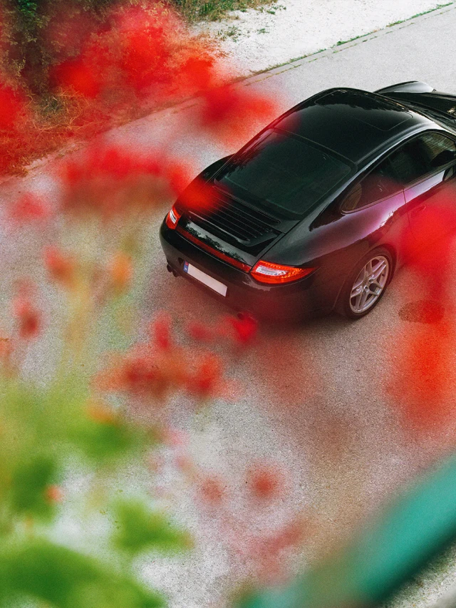 Fekete Porsche 911 felülnézetből, vörös levelekkel az előtérben.