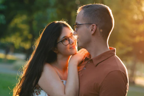 Intimate sunset portrait of a couple wearing glasses as the man kisses the woman on the forehead