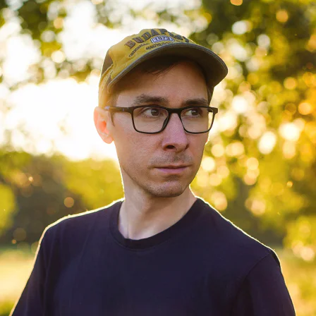 Szabó Roland szemüvegben és baseballsapkában, naplementés parkban.