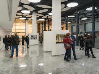 Látogatók beszélgetnek és fényképeket néznek egy modern kiállítótérben.