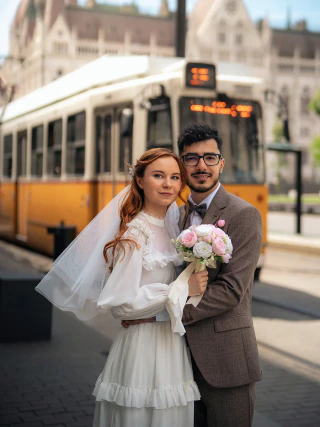 A bride and groom holding a bouquet in front of a yellow tram.
