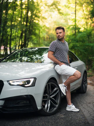 Férfi autós portré egy fehér Audi mellett erdei környezetben
