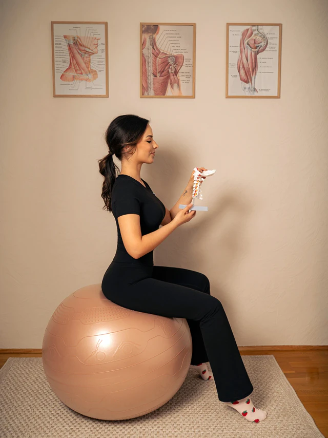 Female brand portrait sitting on an exercise ball while holding a model of a spine