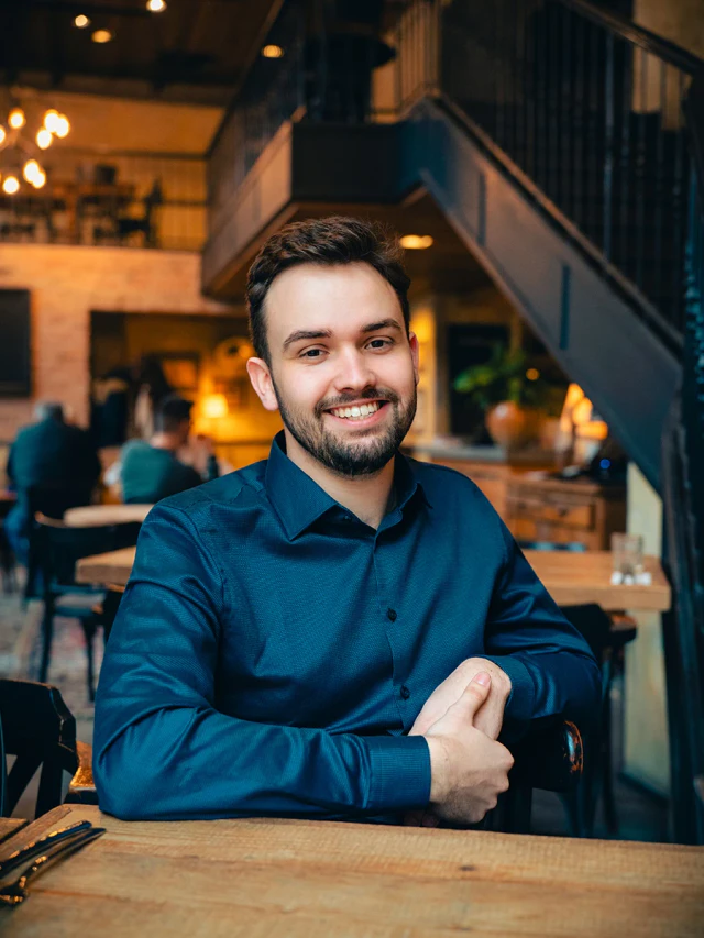 Mosolygó férfi portréja sötétkék ingben, egy hangulatos kávézóban