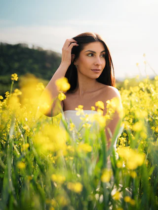 A woman in a white dress posing in a field of yellow flowers