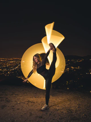 Night portrait of a flexible woman posing above the city with light painting around her