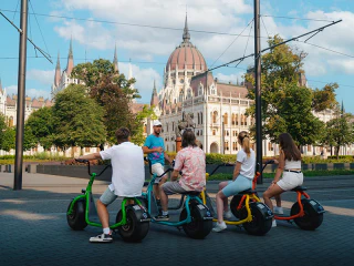 Négy ember színes elektromos rollereken a Parlament előtt.
