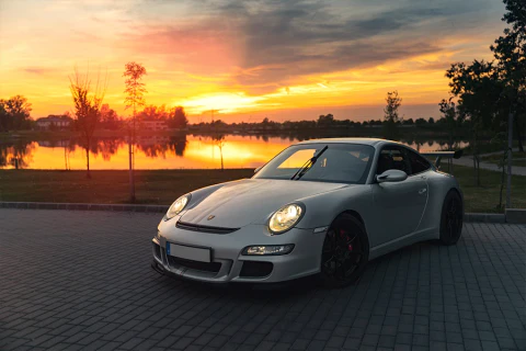 Ezüstszínű Porsche 911 naplementében egy tóparti parkolóban.