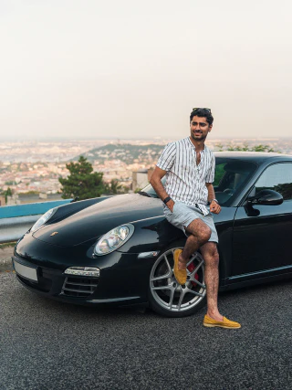 Férfi ül egy fekete Porsche elején, háttérben budapesti panorámával