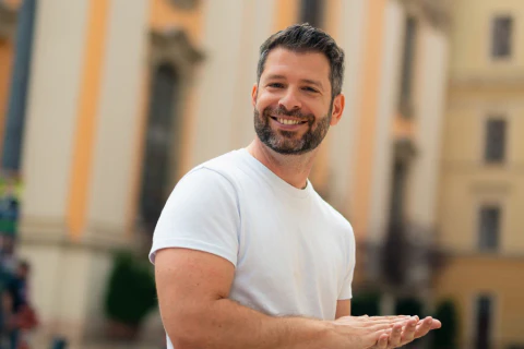 Portrait of a smiling bearded man in a white T-shirt against an urban background
