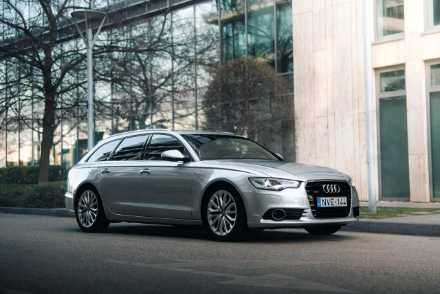 Ezüstszínű Audi A6 Avant egy modern irodaház előtt.