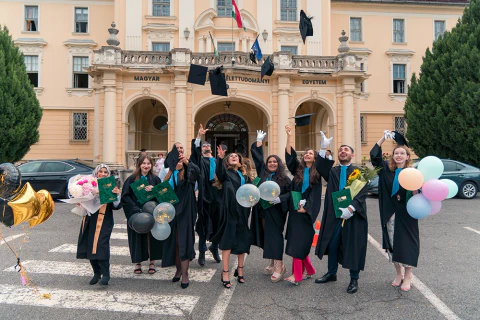 Diplomázók csoportképe lufikkal egy egyetemi épület előtt.
