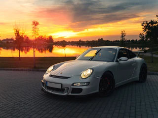 Ezüstszínű Porsche 911 egy tóparti parkolóban, naplementében.