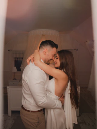 A bride and groom embracing closely in a bedroom.