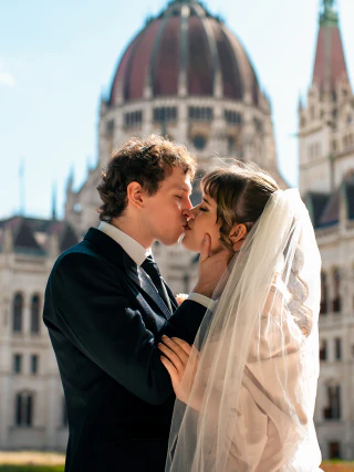 A bride and groom kissing in front of the Hungarian Parliament Building.