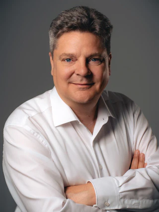 Smiling male business portrait in a white shirt with folded arms against a grey background