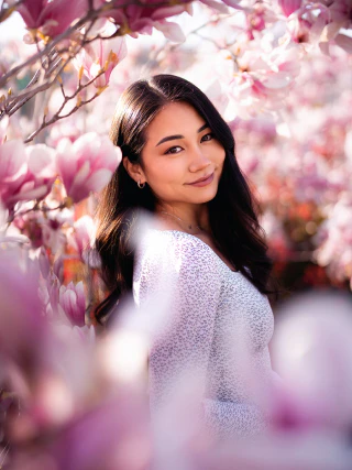 A smiling woman standing among pink magnolia blossoms