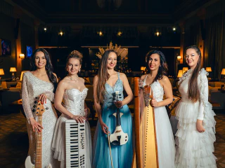 Öt elegánsan öltözött zenész pózol hangszerekkel egy hangulatos beltéri helyszínen.