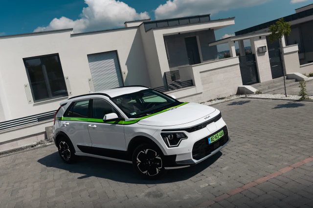 Fehér Kia Niro céges autó egy modern családi ház előtt.