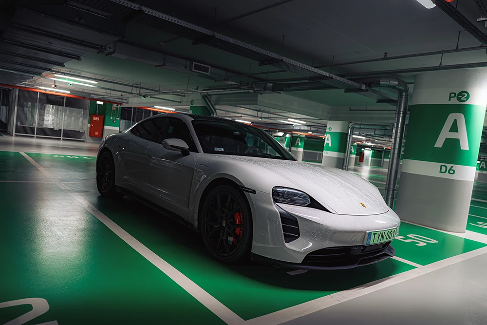 Szürke sportautó egy mélygarázs zöld parkolóhelyén.