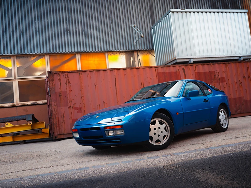 Blue Porsche 944 in front of an old industrial building.