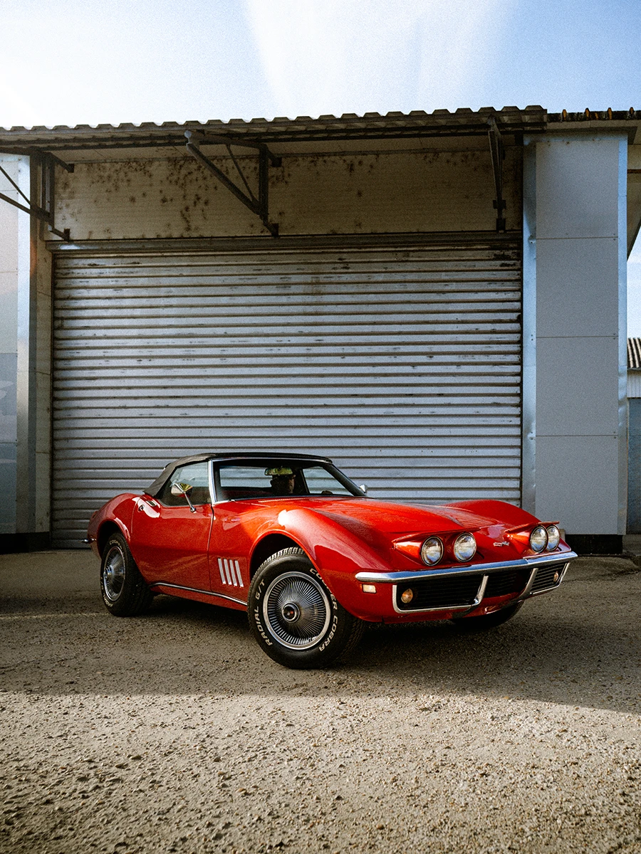 Red Chevrolet Corvette in front of an industrial roller door.