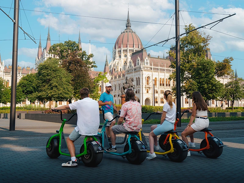 Négy ember színes elektromos rollereken a Parlament előtt.