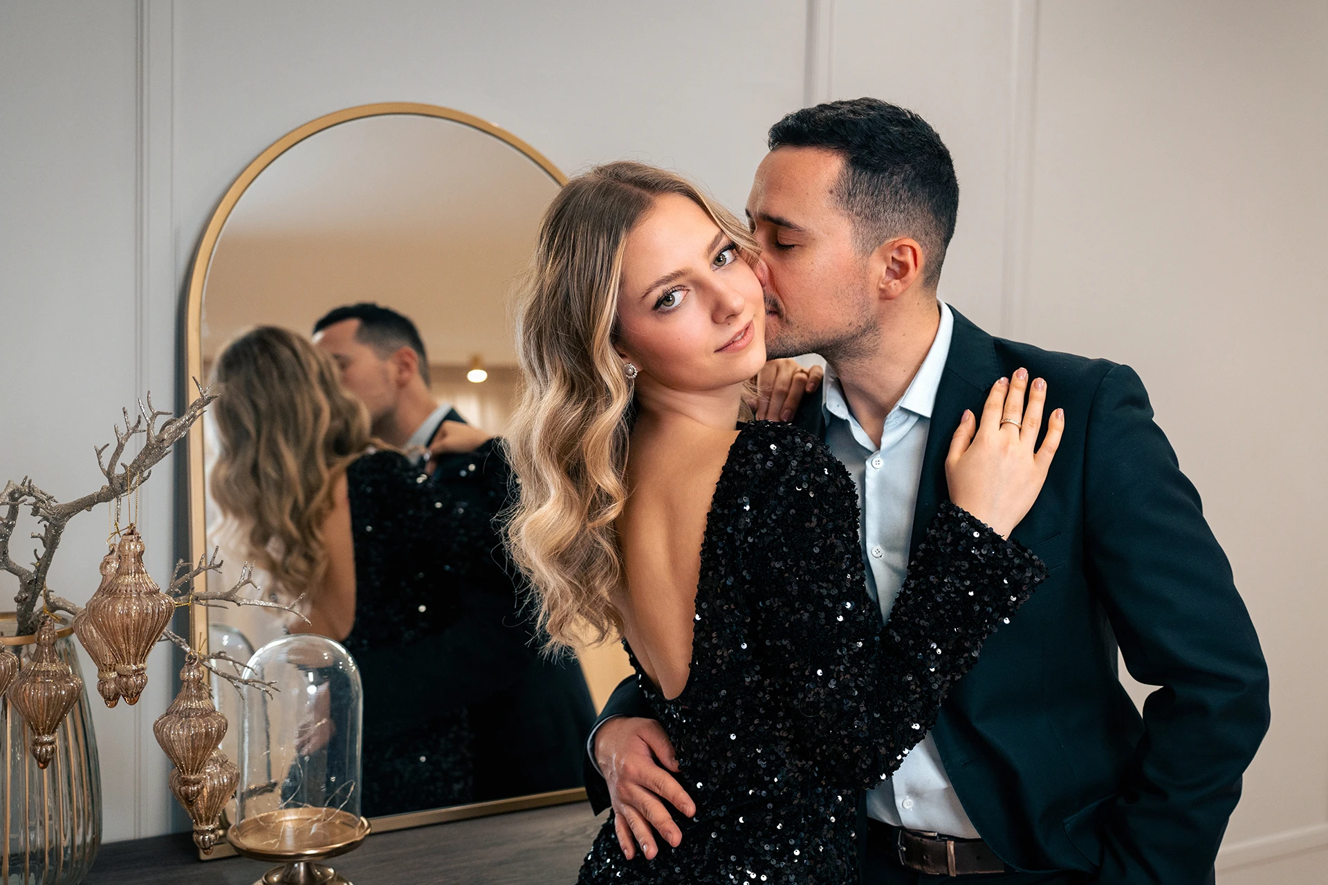 An elegant couple in front of a mirror as the man kisses the woman on the cheek