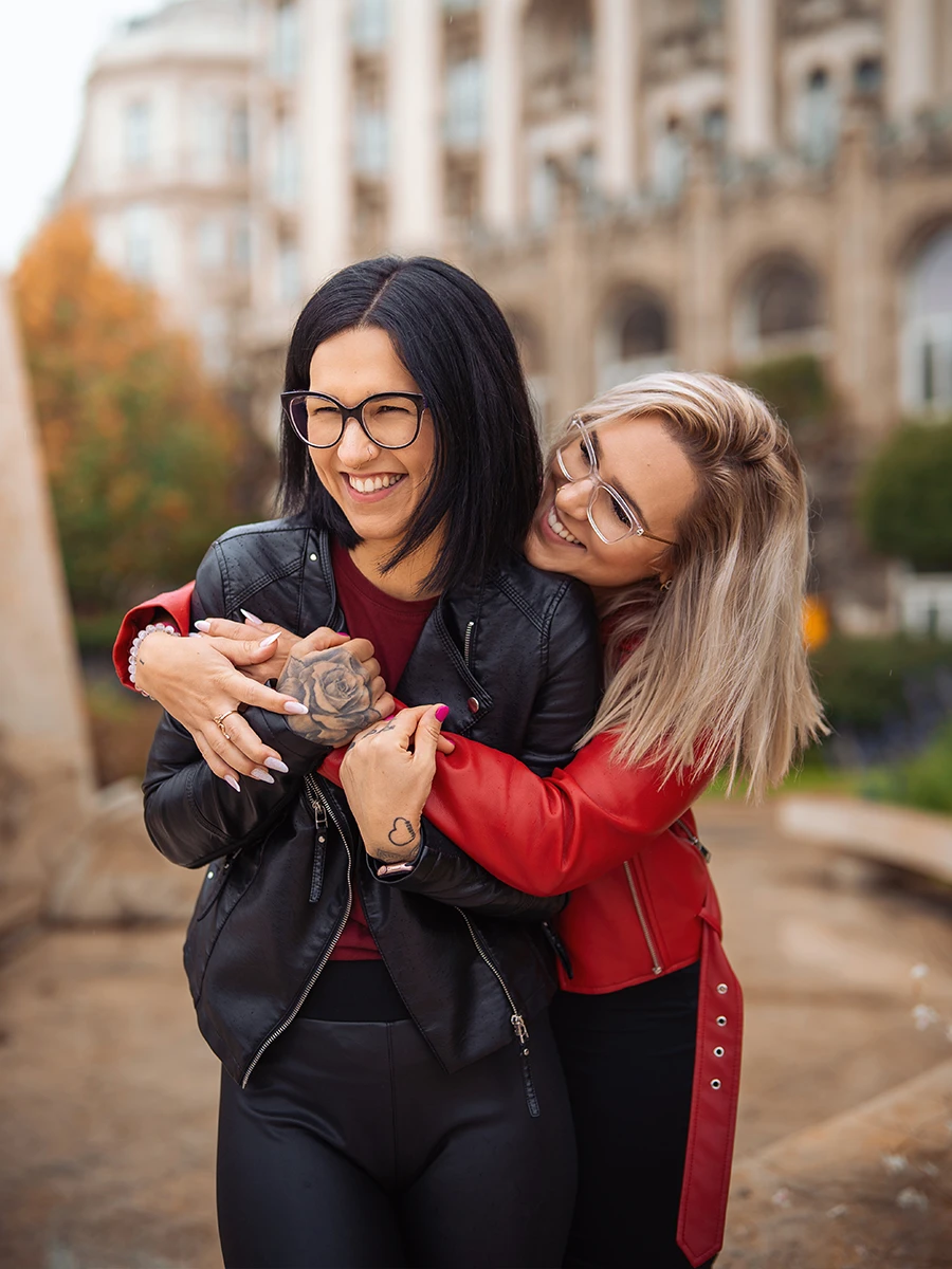Two friends embracing and laughing, one wearing a black coat and the other a red coat